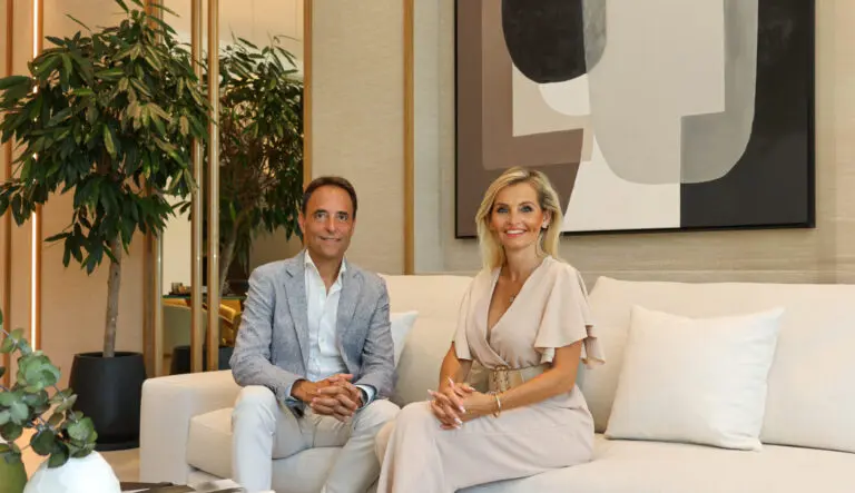 A woman and a man sitting confidently on a couch in a well-appointed living room, conveying a sense of honesty and integrity. The woman, on the right, exudes professionalism, while the man on the left, with a friendly demeanor, represents trusted real estate services.